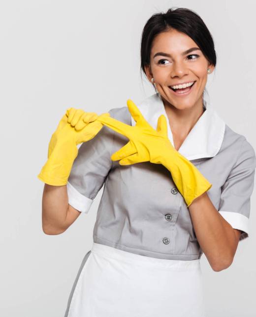 Pretty brunette woman in gray uniform taking off her yellow protective gloves while smiling and looking aside, isolated over white background